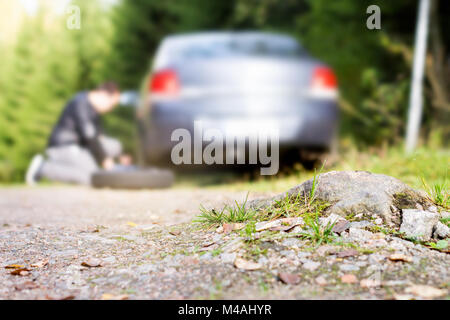 L'uomo modifica nuova ruota di scorta del veicolo dopo aver toccato sulla campagna strada di sabbia. Rotte e piatto di pneumatici vettura in foresta. Driver problema di fissaggio. Foto Stock