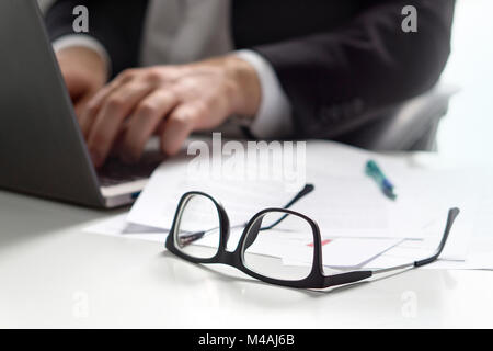 Business man la scrittura con il computer portatile in ufficio con bicchieri sul tavolo. Foto Stock