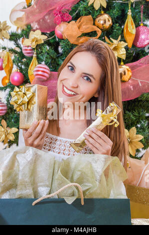 Close up di bella donna sorridente che indossa una camicia bianca nella parte anteriore di un albero di natale, e in possesso di due doni nelle sue mani, merry christmast e felice anno nuovo concetto Foto Stock