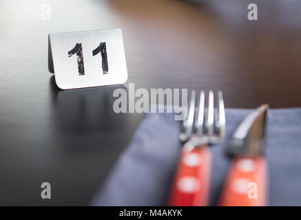 Il segno di numero sul ristorante tabella per mostrare la prenotazione. Utensili, forchetta e coltello nella parte anteriore. In attesa del cliente per il servizio o il cibo. Foto Stock