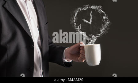 Pausa caffè concetto. Segno di clock dal vapore. La formazione di fumo di un tempo di simbolo. Business man in una tuta in possesso di una bevanda calda in una tazza e tazza da tè. Foto Stock