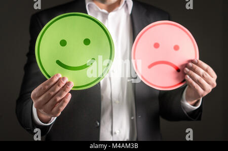 Uomo d affari con sorridenti e triste infelice carta cartone emoticon. Rating e dando recensione sulla soddisfazione del cliente o del team spi Foto Stock