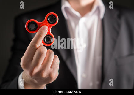 Uomo d'affari con un agitano: spinner. Imprenditore in un vestito tenendo trendy kids ansia sollievo giocattolo in mano. Foto Stock