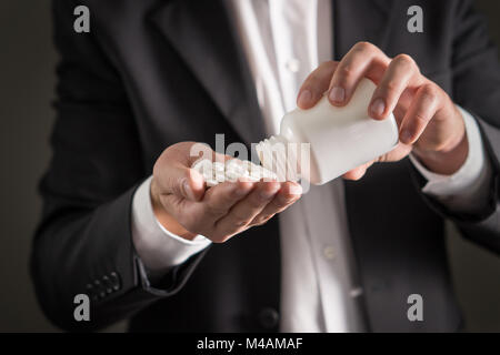 Rappresentante farmaceutica, consulente o testa direttore o manager della società di medicina con compresse di colore bianco. Uomo in una tuta versando la fuoriuscita di pillole. Foto Stock