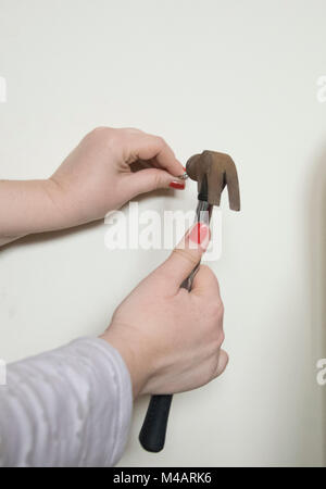 Una chiusura di un womans mani con unghie rosse e un martello Foto Stock