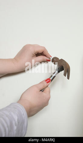 Una chiusura di un womans mani con unghie rosse e un martello Foto Stock