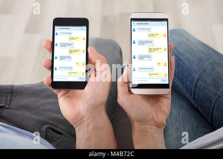 Close-up del giovane mano sta tenendo i telefoni cellulari che mostra i messaggi sullo schermo Foto Stock