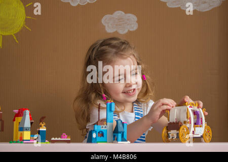 Carino divertente preschooler bambina gioca con la costruzione di blocchi giocattolo in asilo nido stanza. sfondo dipinto dal sole e nuvole Foto Stock