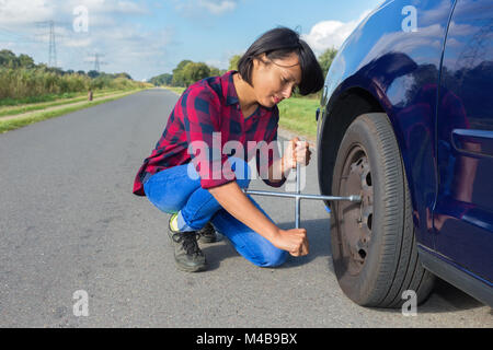 Giovane donna cambiare auto ruota sulla strada di campagna Foto Stock