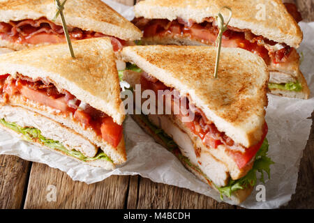 Livello club sandwich con carne di tacchino, pancetta, pomodori e lattuga macro su carta. orizzontale Foto Stock