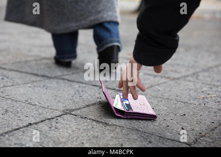 In prossimità di un uomo di prelevare un portamonete perduto sulla strada Foto Stock