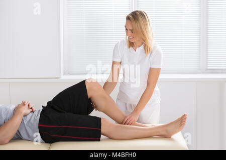 Donna sorridente fisioterapista dando la terapia del ginocchio per un uomo in clinica Foto Stock