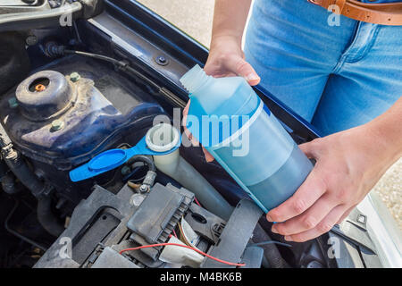 Donna di riempimento serbatoio auto con fluido blu in bottiglia Foto Stock