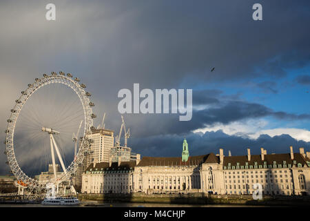 Londra, Regno Unito. Xi Febbraio, 2018. Colpisce nel tardo pomeriggio sole cade sulla County Hall e per il London Eye contro uno sfondo di nuvole scure. Foto Stock