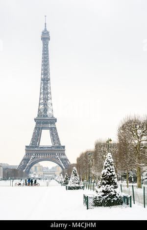Inverno a Parigi nella neve. La torre Eiffel si vede dal Champ de Mars con prato e abeti coperti di neve in primo piano. Foto Stock