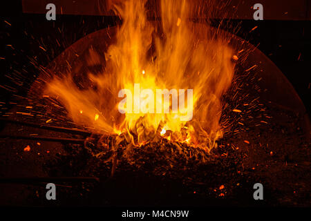 Hot fabbro forgiare con carboni ardenti e le scintille Foto Stock