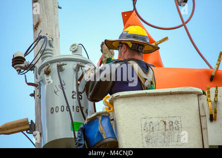 Un lineman riparazioni apparecchiature elettriche su un polo utilità lavorando da un elevato della piattaforma di lavoro chiamato anche un cherry picker. Foto Stock