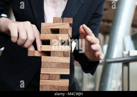 Imprenditrice mano tirare fuori il blocchetto in legno dalla torre. crescita, rischio e strategia aziendale. Foto Stock