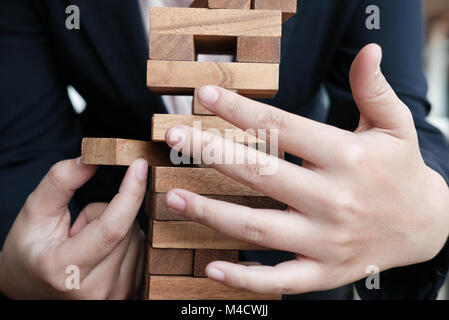 Imprenditrice mano tirare fuori il blocchetto in legno dalla torre. crescita, rischio e strategia aziendale. Foto Stock