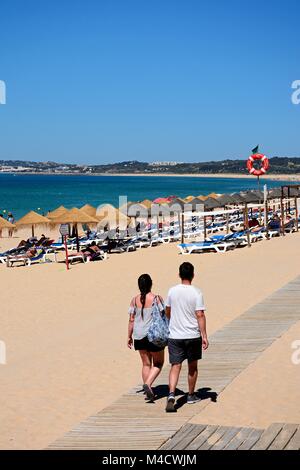 I turisti a piedi lungo una passerella in spiaggia con la gente a prendere il sole per la parte posteriore e vedute sull'oceano, Praia da Rocha, Algarve, Portogallo, dell'Europa. Foto Stock