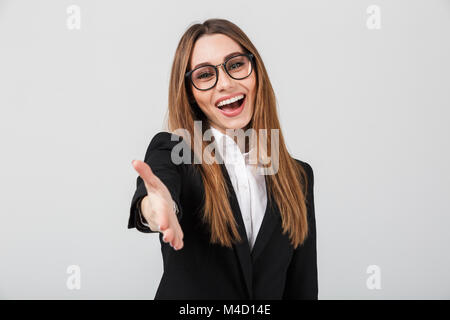 Ritratto di un amichevole imprenditrice vestito in tuta in piedi con la mano tesa per il messaggio di saluto isolate su uno sfondo grigio Foto Stock