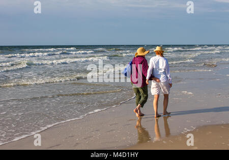 Due americani senior citizen donne camminano insieme su una spiaggia nelle prime ore del mattino. Foto Stock