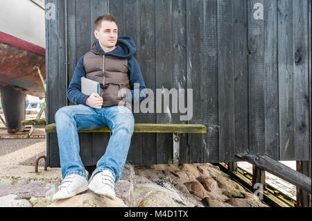 Uomo seduto su una panchina nella parte anteriore della parete in legno Foto Stock