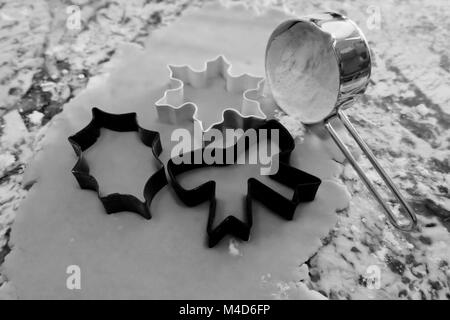 Tre natale cookie cutters accanto a farina in bianco e nero. Foto Stock