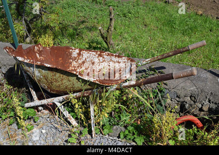 Vecchio rotto e rusty carriola abbandonato su un prato Foto Stock