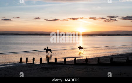 Delle cavalcate sulla spiaggia al tramonto Foto Stock