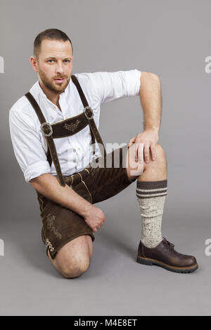 L uomo nella tradizionale bavarese lederhosen inginocchiato Foto Stock