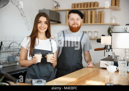 Caffè il concetto di Business - Positivo giovane uomo barbuto e bella attraente dama barista giovane dando take away tazza di caffè al customer presso la moderna caffetteria Foto Stock