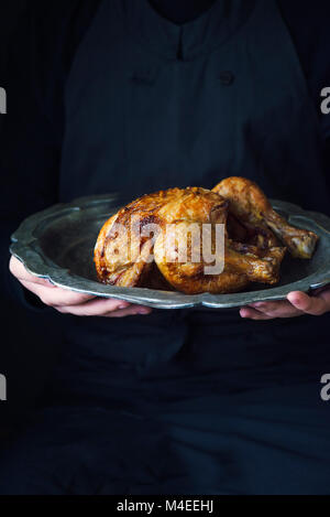 Persona in possesso di un pollo arrosto su di una piastra in peltro Foto Stock