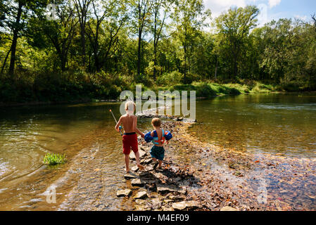 Due ragazzi che attraversa un fiume per andare a pesca Foto Stock