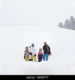 Famiglia in piedi nella neve tenendo lo snowboard e lo slittino Foto Stock