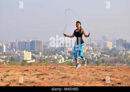 Athletic donna esercita con corda da salto con sfondo di montagne di Pune, Maharashtra. Foto Stock