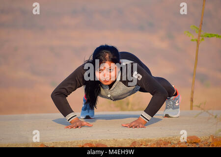 Giovane ragazza indiana facendo push-up con sfondo di montagne di Pune, Maharashtra. Foto Stock