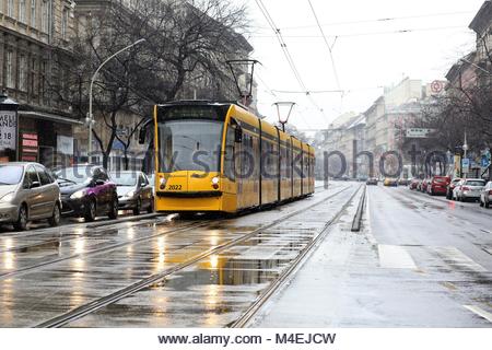 Un giallo il tram passa attraverso una strada principale molto trafficata a Budapest, in Ungheria su una giornata invernale e. Foto Stock