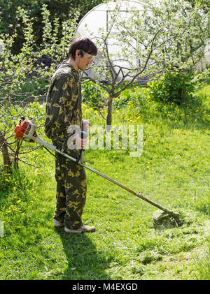 L'uomo mows l'erba nel suo giardino Foto Stock