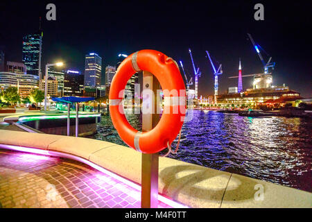 Red salvagente sul primo piano sul marciapiede di Elizabeth Quay Marina nel centro di Perth, Western Australia. Esplanade e la costruzione di gru su sfondo sfocato. Perth città capitale di notte. Foto Stock