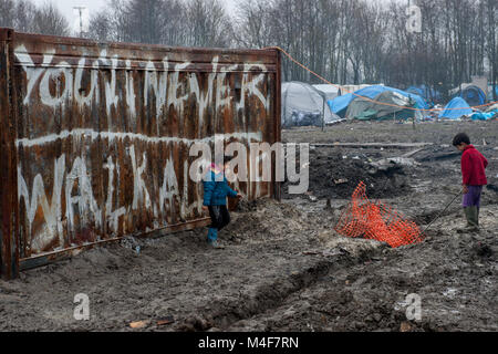 Grande-Synthe, nel nord della Francia. Il 31 gennaio 2016. I bambini giocano accanto a una formazione di ruggine contenitore di spedizione. Il Grande-Synthe Refugee Camp vicino al porto di Dunkerque in Francia settentrionale. Nel campo condizioni sono grim in parte a causa di fango spesso e la mancanza di servizi di base. Le famiglie vivono in pioggia inzuppato tende e stringersi intorno a piccoli incendi per il calore base. Foto Stock