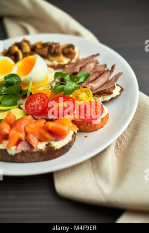 La bruschetta, assortiti, diversi ripieni, su piastre con un soft-uovo sodo in medio Foto Stock