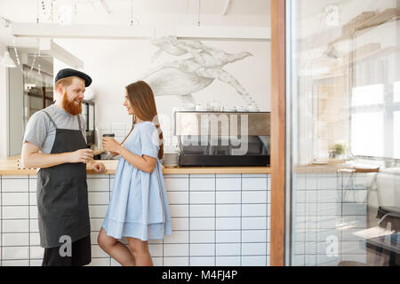 Caffè il concetto di Business - giovani smart barbuto barista godere di parlare e dare portar via tazza di caffè per piuttosto cliente. Foto Stock
