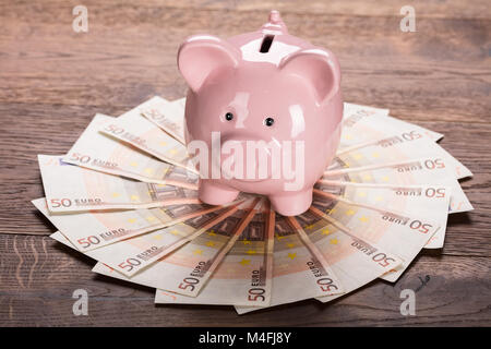 Close-up di un Piggybank su Euro nota alla scrivania in legno Foto Stock