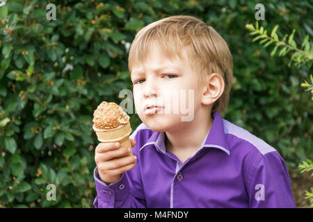 Ragazzo biondo sono mangiare gelato con mettere la lingua di fuori Foto Stock