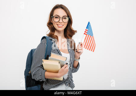 Ritratto di una sorridente ragazza casual studente con zaino contenere libri e bandiera americana isolate su sfondo bianco Foto Stock