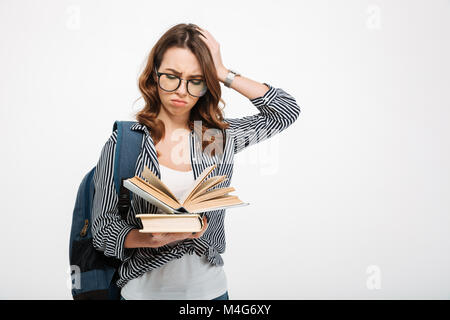 Ritratto di un confuso informale una studentessa con zaino libri di lettura permanente, mentre libri isolate su sfondo bianco Foto Stock