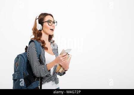 Immagine di scioccato sorpreso giovane e bella signora in piedi isolate su muro bianco sfondo utilizzando il telefono cellulare ascoltando la musica. Guardando a parte. Foto Stock