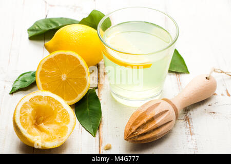 Limonata naturale con legno alesatore e limone foglie su un bianco tavolo in legno Foto Stock