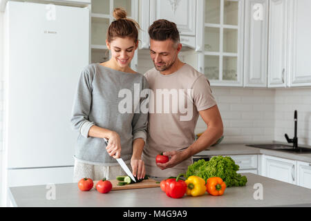Ritratto di un sorridente amare giovane insalata di cottura insieme mentre in piedi su una cucina a casa, la donna come tagliare le verdure Foto Stock